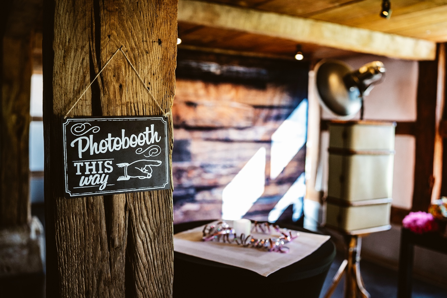 Schild Photobooth this way am Holzbalken und der Bilderkoffer im Hintergrund